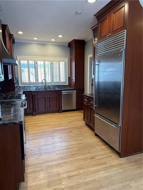 Kitchen with dark stone countertops, a sink, stainless steel dishwasher, fridge, and crown molding