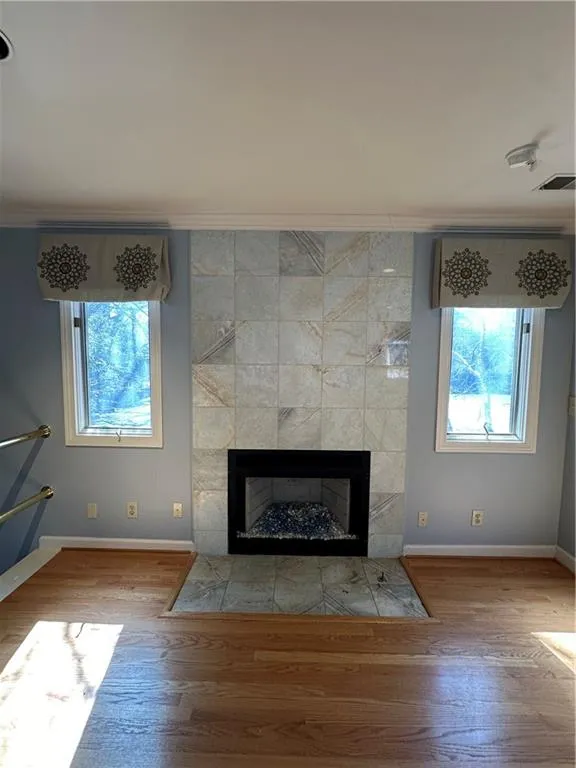 Room details featuring visible vents, wood finished floors, crown molding, baseboards, and a tile fireplace