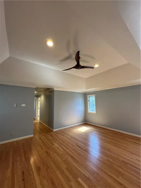 Unfurnished room with baseboards, lofted ceiling, a tray ceiling, wood finished floors, and a ceiling fan