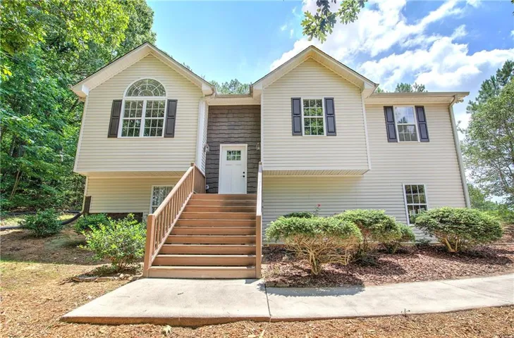 Split-level residence featuring light-colored siding, a prominent wood staircase, and dark accent shutters