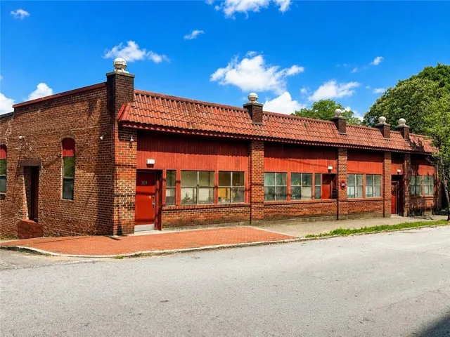 Brick facade building featuring a red tile roof, multiple large windows, a prominent red entry door, and a brick paver walkway