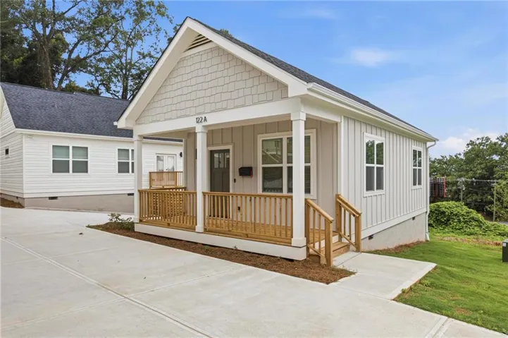 Contemporary bungalow featuring a covered front porch with natural wood railings, board and batten siding, and architectural shingles
