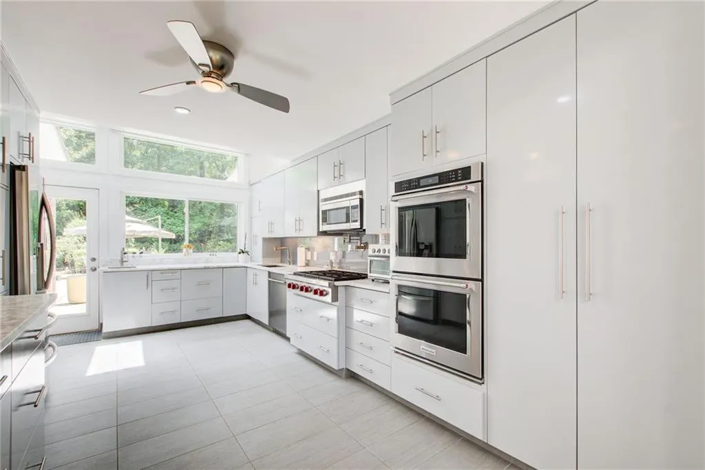 Kitchen featuring light tile patterned flooring, white cabinetry, ceiling fan, stainless steel appliances, and backsplash