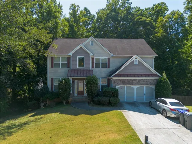 Two-story residence featuring light-toned siding, a two-car garage with arched window details, a covered entryway with a transom window, and a sloped, paved driveway