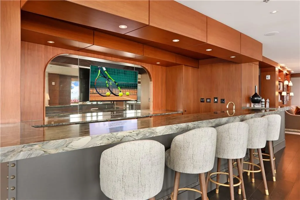 Indoor wet bar with dark wood finished floors, recessed lighting, wooden walls, and stone counters