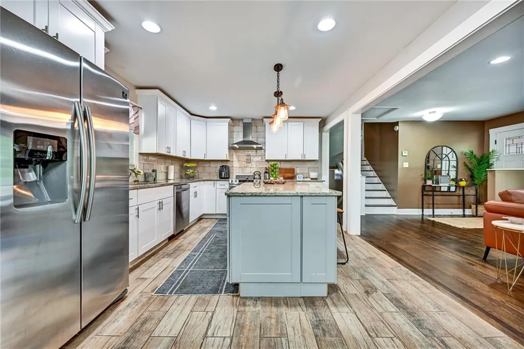 Kitchen with pendant lighting, wall chimney exhaust hood, white cabinetry, stainless steel appliances, and light hardwood / wood-style floors