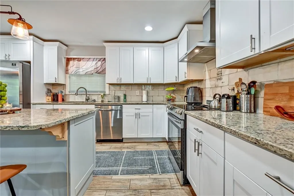 Kitchen featuring light stone counters, wall chimney range hood, white cabinetry, stainless steel appliances, and a breakfast bar area