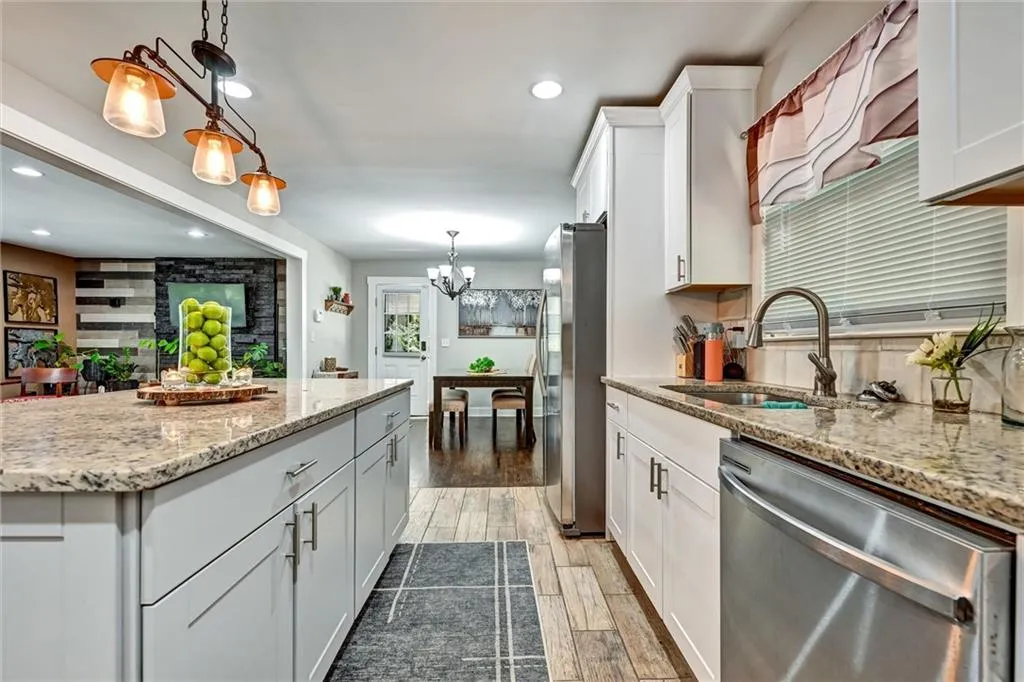 Kitchen with white cabinets, hanging light fixtures, sink, appliances with stainless steel finishes, and dark hardwood / wood-style floors