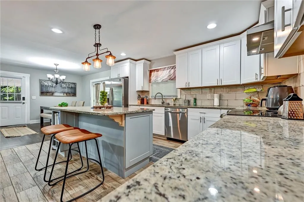 Kitchen with a kitchen island, light stone counters, white cabinets, appliances with stainless steel finishes, and hardwood / wood-style flooring