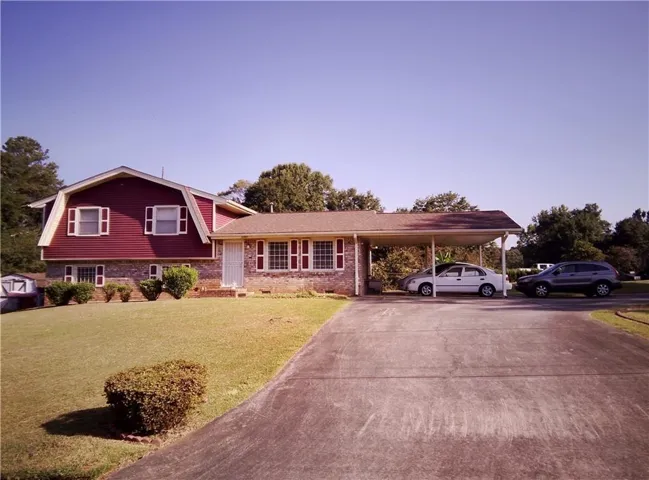 Red siding exterior with stone accents, covered carport, and a concrete driveway