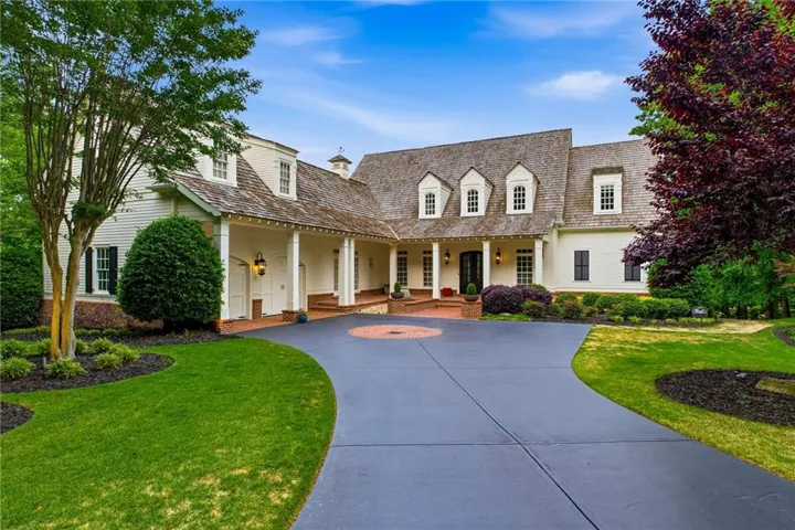 Expansive paved driveway with decorative brick inlay, shuttered windows, multiple dormers, and a covered entry