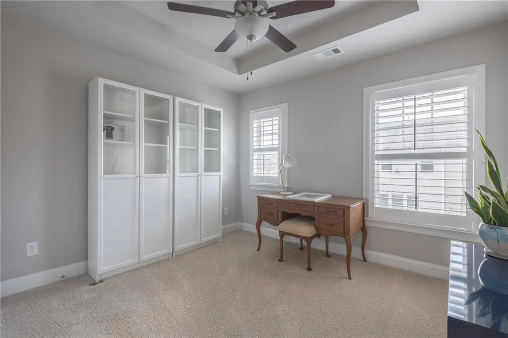 Office with ceiling fan, carpet flooring, and a raised ceiling