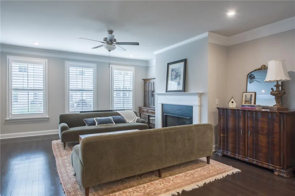 Living room featuring a ceiling fan, a fireplace, dark wood finished floors, ornamental molding, and recessed lighting