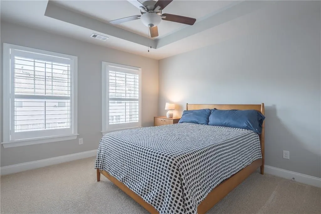 Carpeted bedroom with a tray ceiling and ceiling fan
