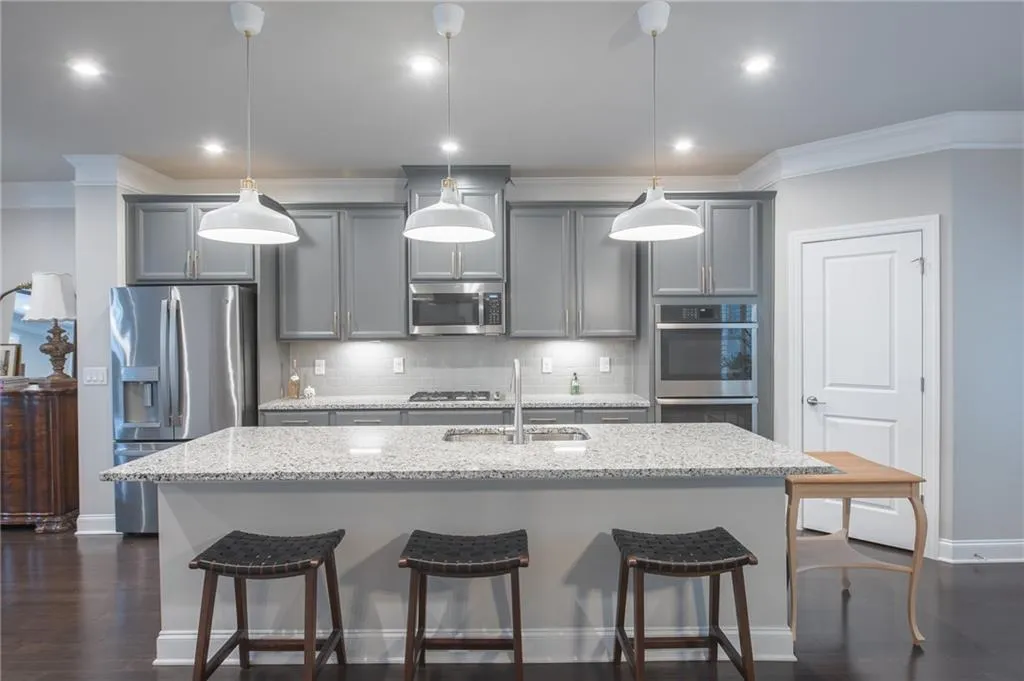 Kitchen featuring gray cabinets, appliances with stainless steel finishes, a kitchen bar, a center island with sink, and crown molding