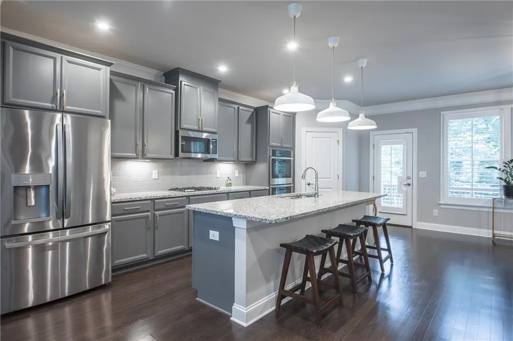 Kitchen with stainless steel appliances, gray cabinets, a center island with sink, ornamental molding, and a breakfast bar area