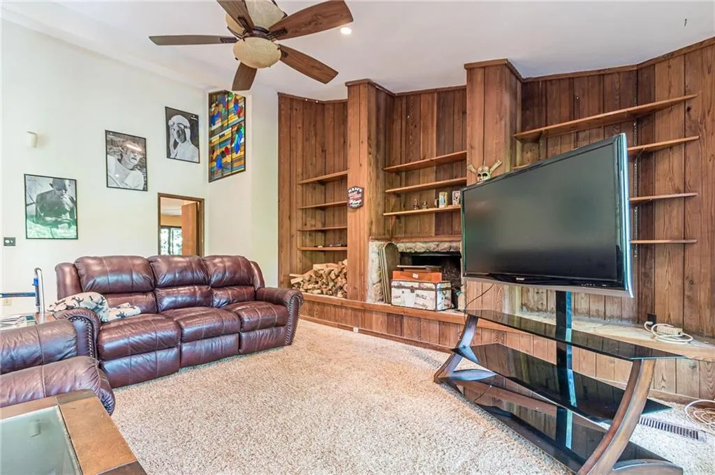 Carpeted living room featuring wooden walls and ceiling fan