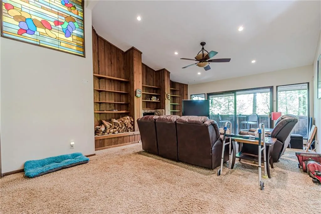 Carpeted living room with wooden walls, built in shelves, vaulted ceiling, and ceiling fan