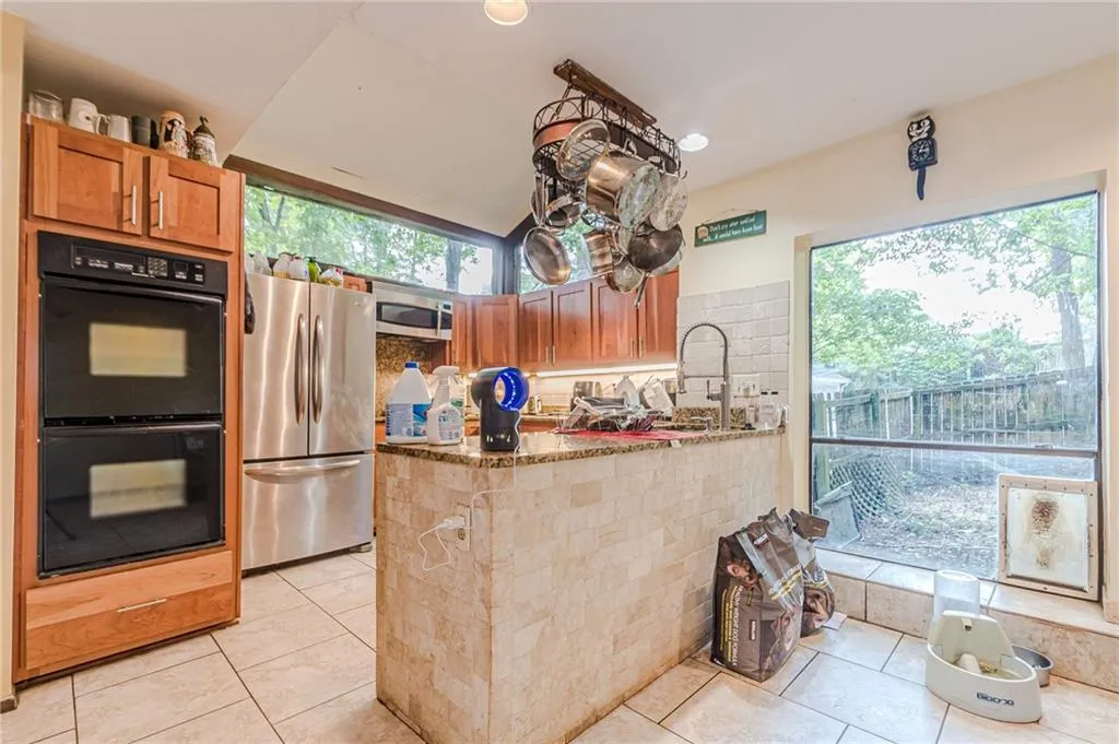 Kitchen with stone counters, stainless steel appliances, kitchen peninsula, backsplash, and light tile patterned flooring