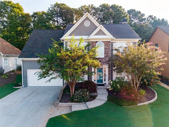 Two-story residence featuring a stone and siding exterior, an attached garage, a concrete driveway, and mature landscaping