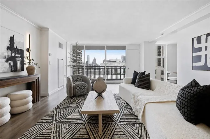 Wood-finish flooring throughout, bright white walls, crown molding, and floor-to-ceiling glass doors opening to a balcony with a black metal railing