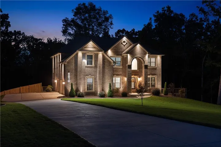 Brick exterior with architectural accent lighting, arched entryway, gabled roofline, and an attached garage