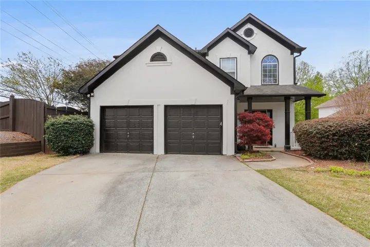 Stucco exterior featuring black trim accents, a two-car garage with dark paneled doors, a covered entry porch with black support columns, an arched window on the upper level, and a concrete driveway