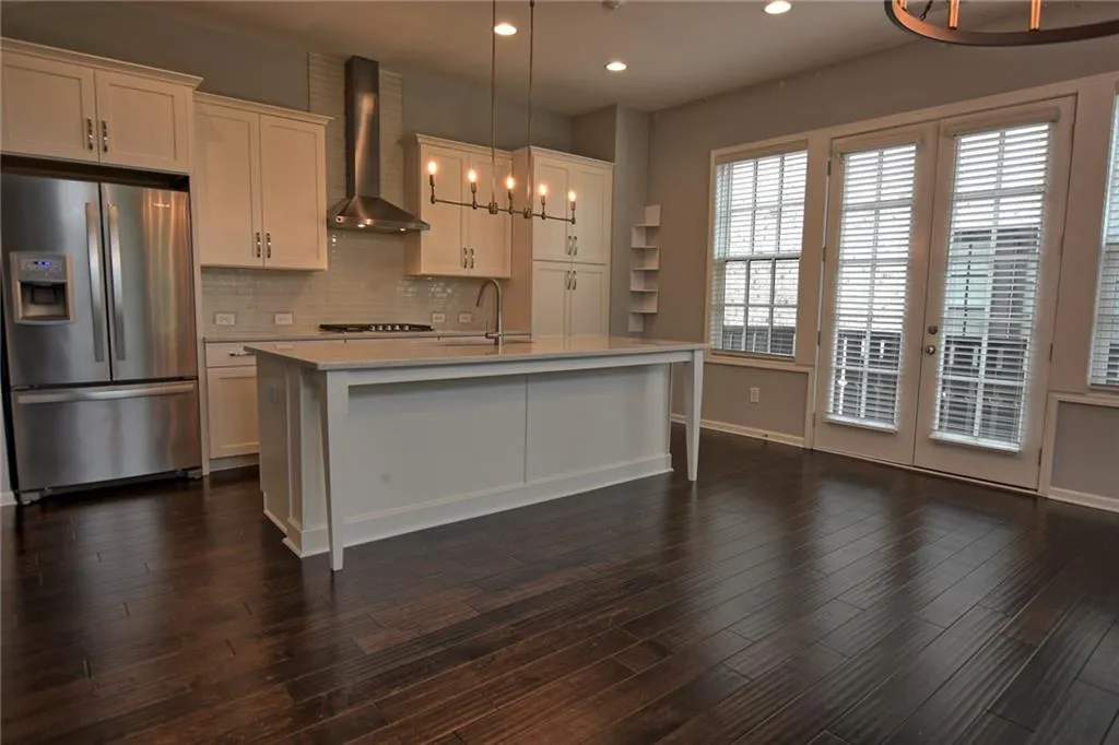 Kitchen featuring a notable chandelier, a sink, stainless steel fridge with ice dispenser, light countertops, and wall chimney exhaust hood