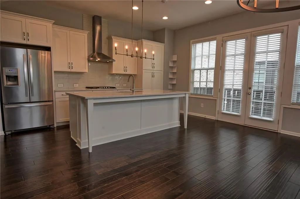 Kitchen featuring light countertops, stainless steel fridge with ice dispenser, a sink, a chandelier, and wall chimney exhaust hood