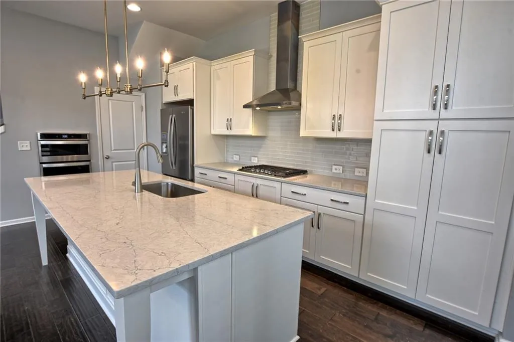 Kitchen featuring an island with sink, wall chimney range hood, a sink, dark wood finished floors, and appliances with stainless steel finishes