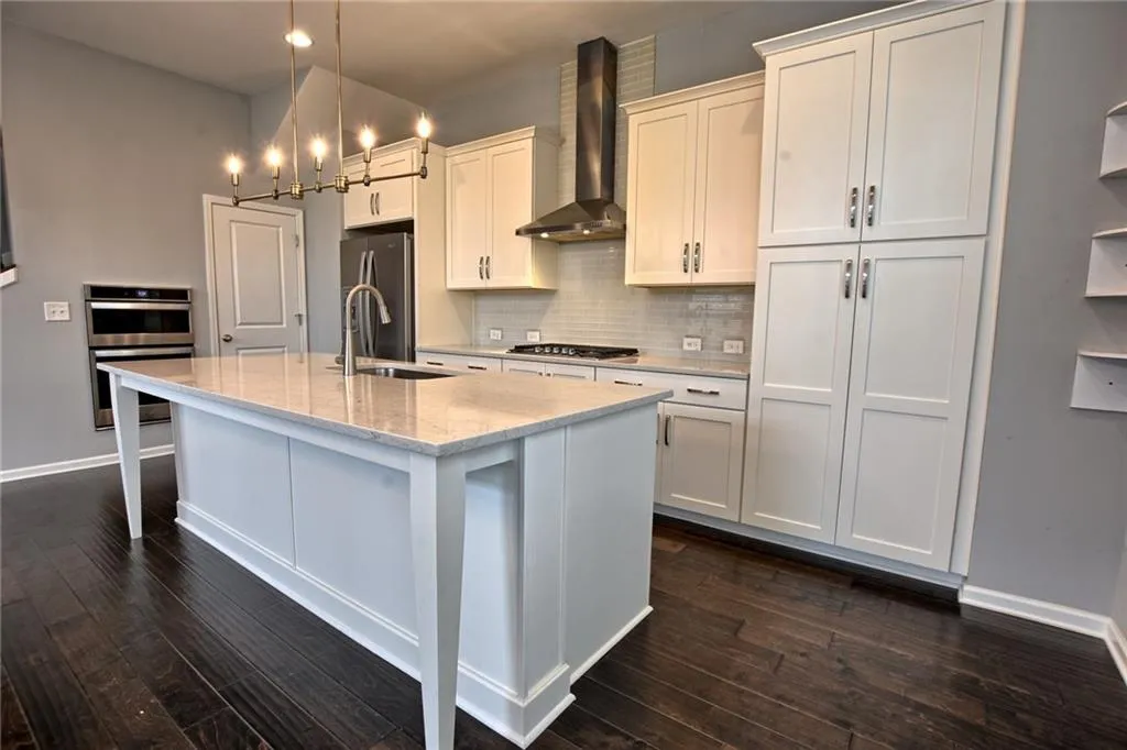 Kitchen featuring wall chimney range hood, appliances with stainless steel finishes, a center island with sink, and dark wood-style floors