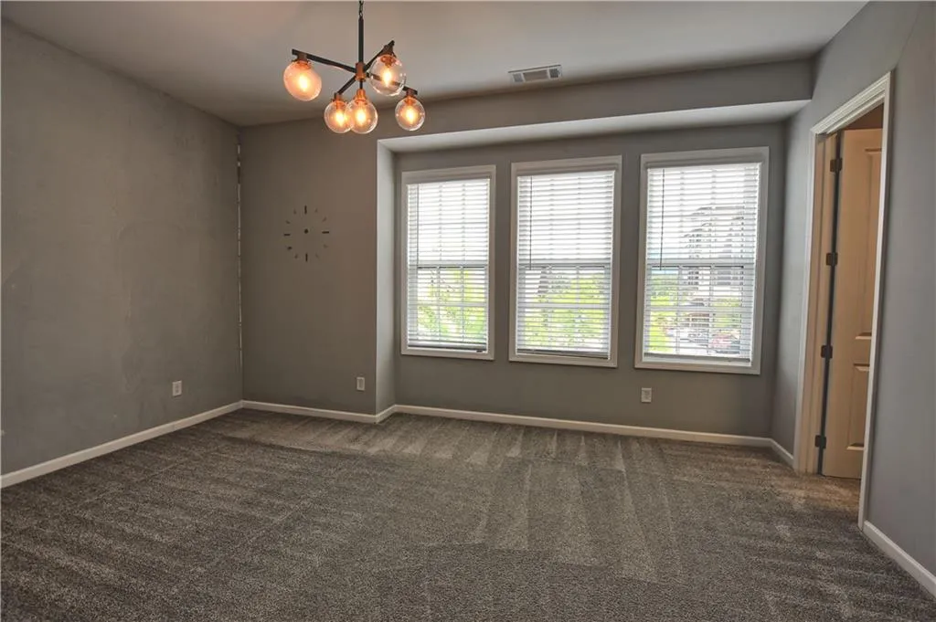 Empty room with a wealth of natural light, dark carpet, and visible vents