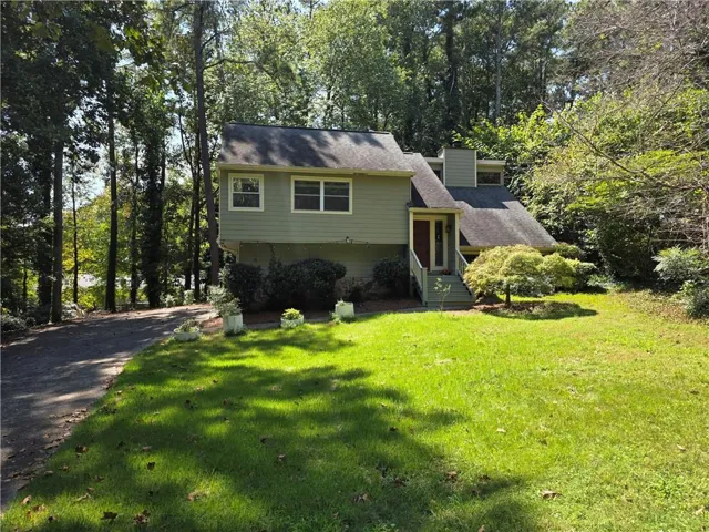 Split-level residence featuring a prominent front entrance with stairs, a paved driveway, and established landscaping