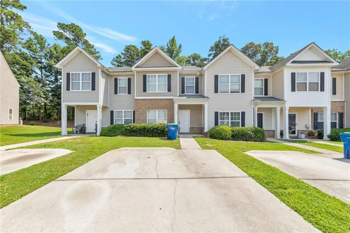 Townhome exterior featuring light-colored siding, dark window shutters, and a partial brick facade