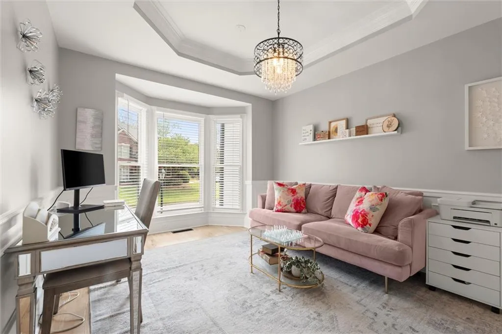 Office space with hanging lights, ornamental molding, light wood finished floors, and a tray ceiling
