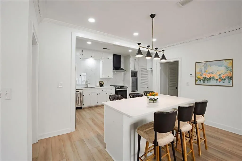 Kitchen featuring ornamental molding, appliances with stainless steel finishes, light wood finished floors, light countertops, and a breakfast bar