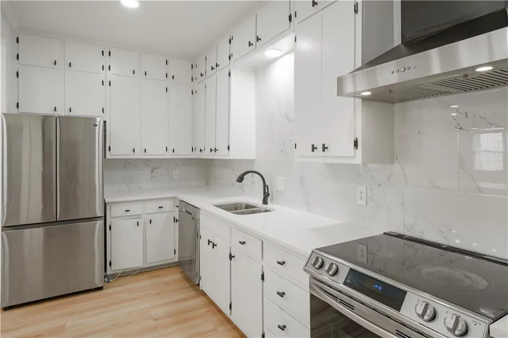Kitchen featuring appliances with stainless steel finishes, extractor fan, decorative backsplash, white cabinets, and light wood-type flooring