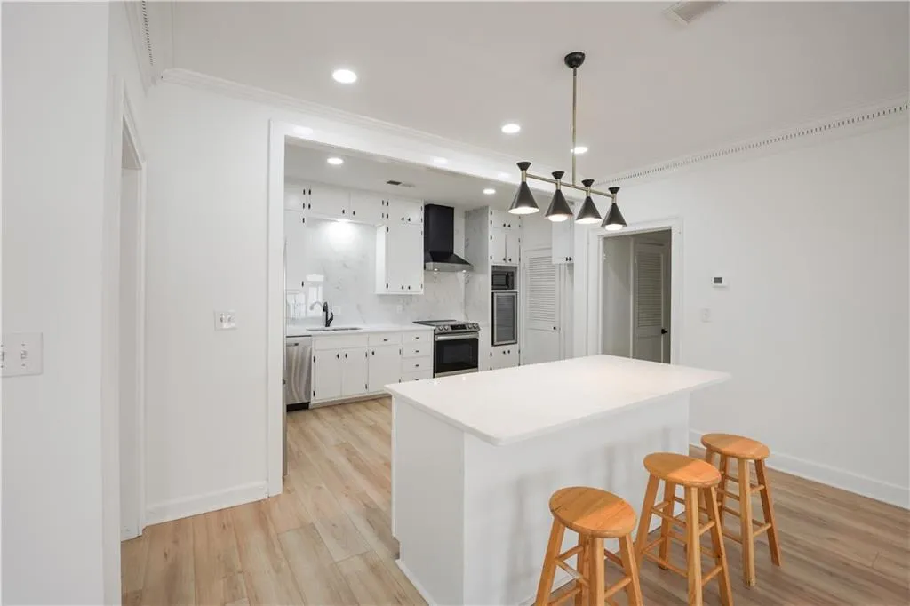 Kitchen with white cabinets, a breakfast bar, light countertops, tasteful backsplash, and ornamental molding