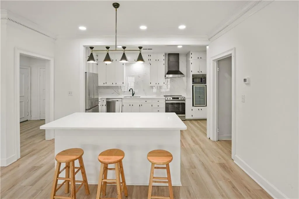 Kitchen featuring white cabinetry, light countertops, decorative light fixtures, a kitchen breakfast bar, and wall chimney exhaust hood