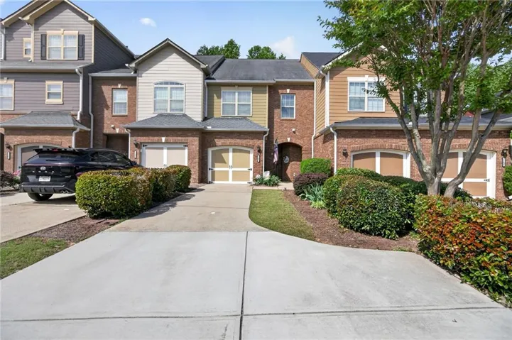 Brick and siding townhome featuring a concrete driveway, two-car garage, and mature landscaping