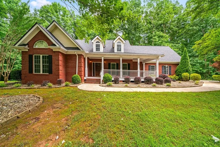 Brick exterior home featuring a covered front porch with white columns, dormer windows, and a curved concrete walkway