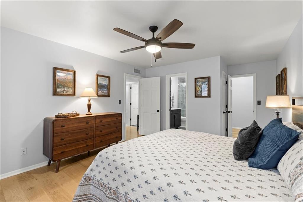 Primary bedroom featuring hardwood flooring, ceiling fan, and ensuite bathroom