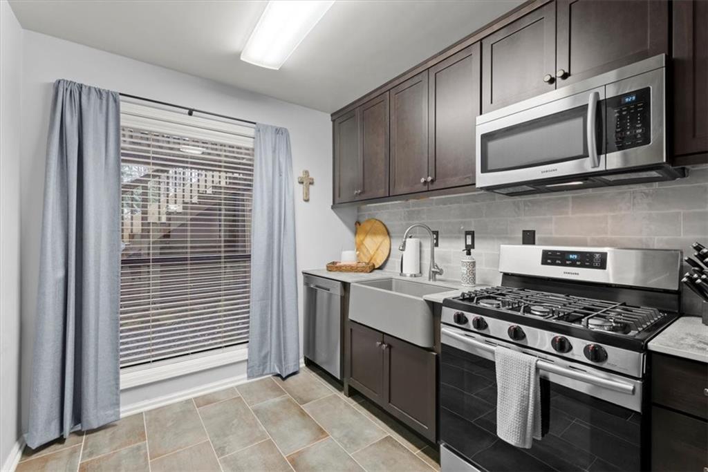 Kitchen with backsplash, dark brown cabinets, sink, stainless steel appliances, and light tile flooring