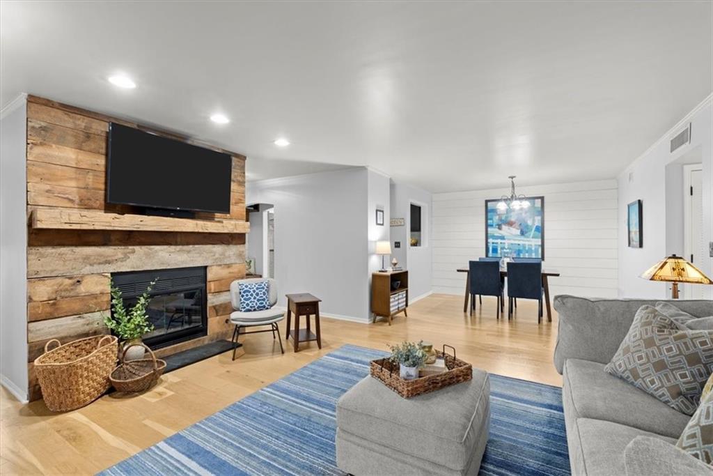Living room with wooden accent wall, a fireplace, crown molding, light hardwood flooring, and a notable chandelier