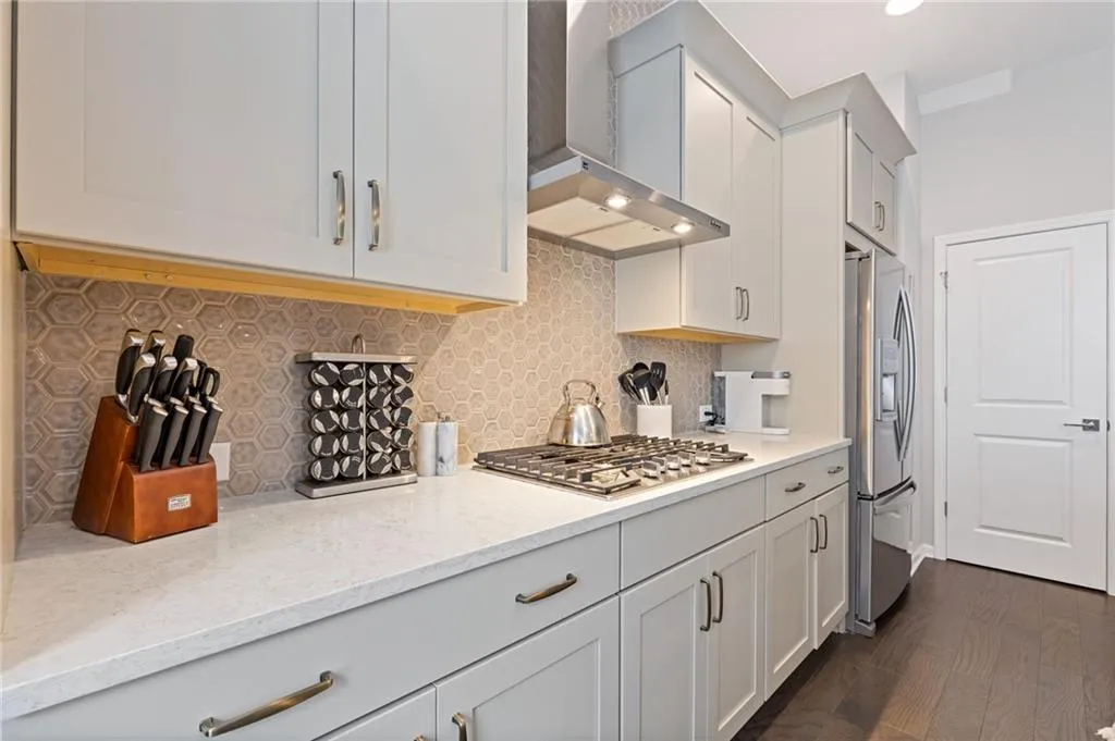 Kitchen featuring tasteful backsplash, wall chimney range hood, appliances with stainless steel finishes, light stone counters, and dark wood-type flooring