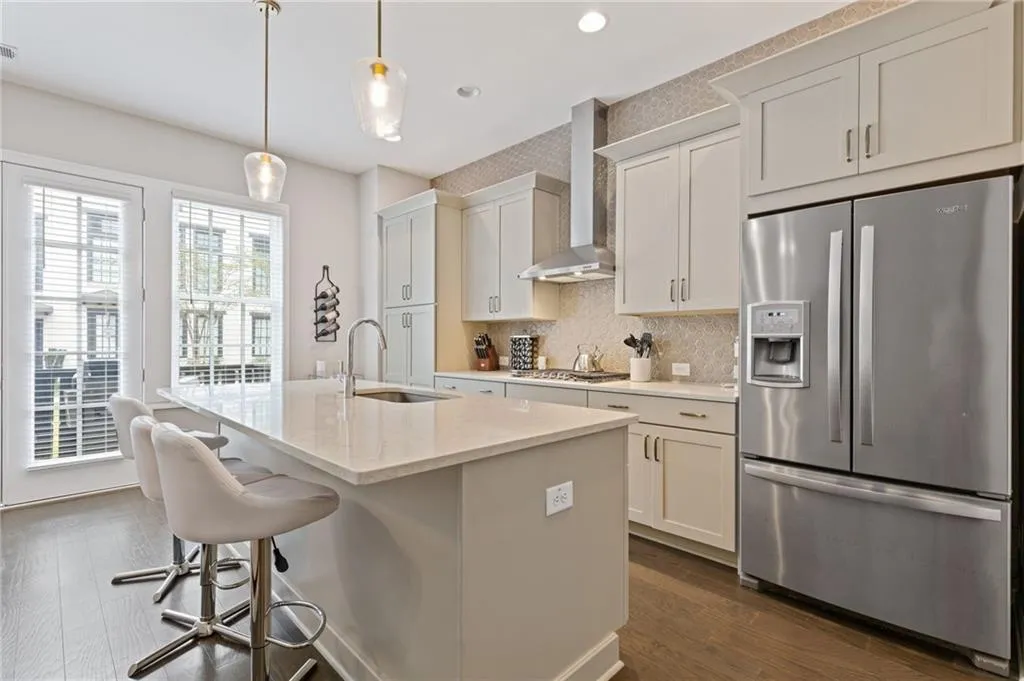 Kitchen with stainless steel appliances, wall chimney exhaust hood, backsplash, dark wood-style flooring, and pendant lighting