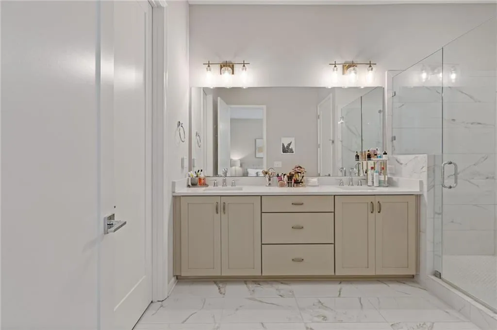 Full bath with light marble finish floors, a marble finish shower, and double vanity