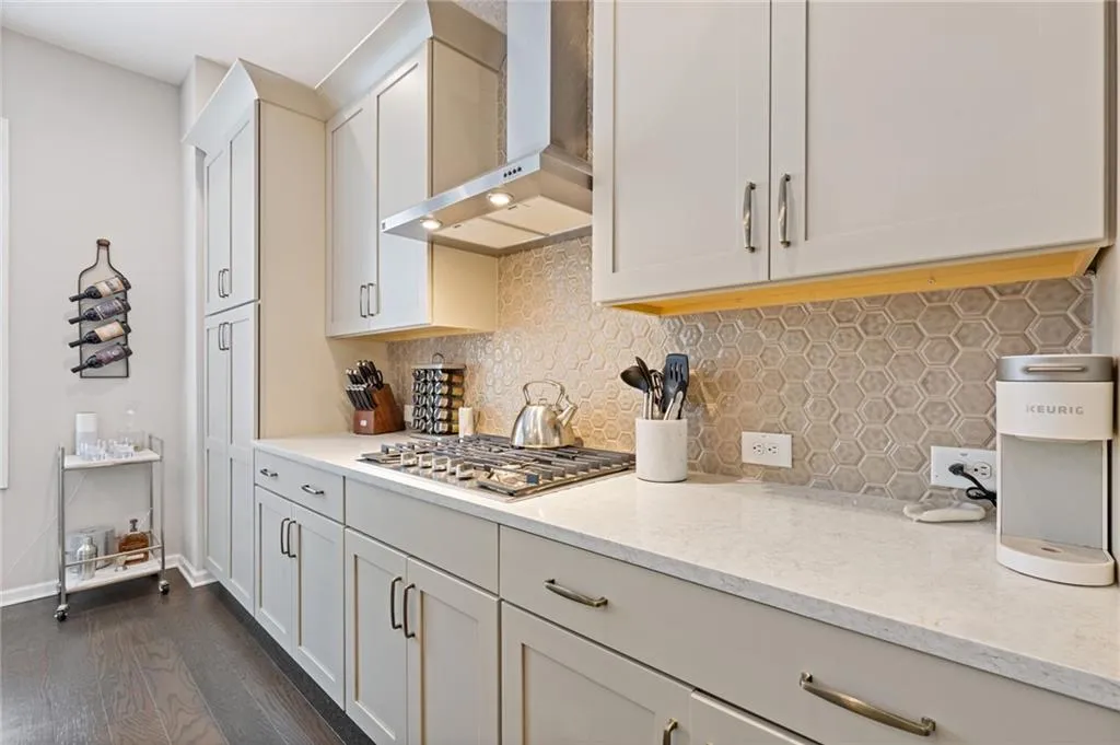 Kitchen with wall chimney range hood, tasteful backsplash, dark wood finished floors, light stone countertops, and stainless steel gas stovetop