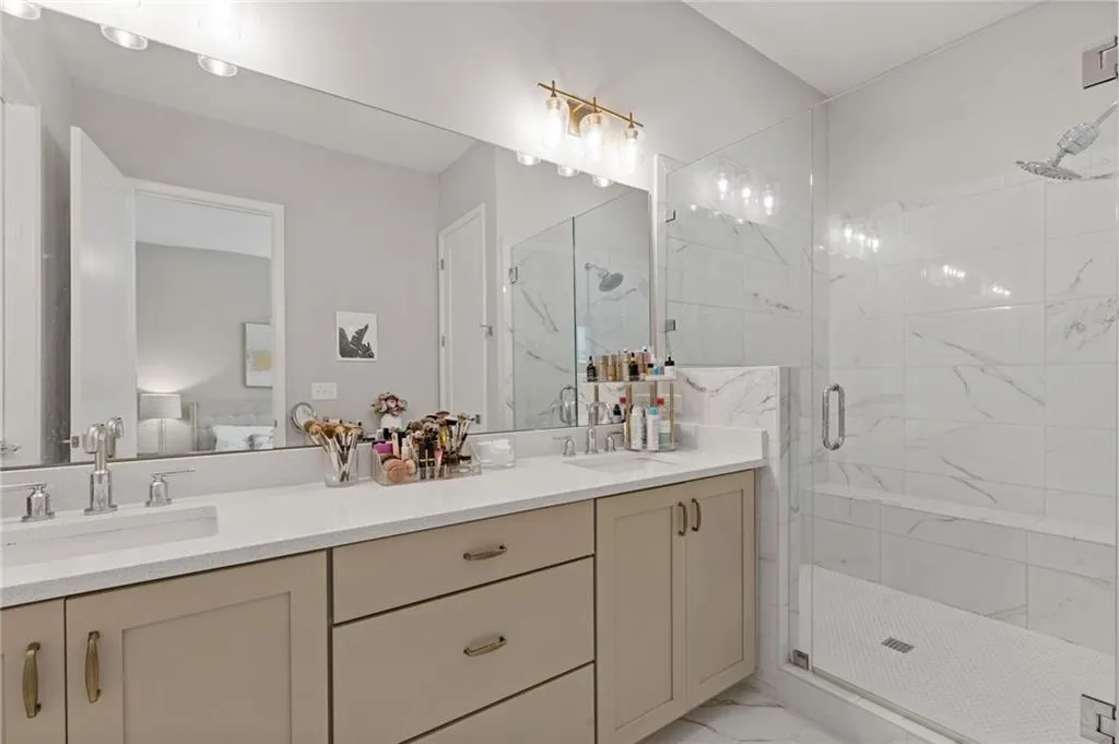 Ensuite bathroom featuring a marble finish shower, light marble finish floors, and double vanity