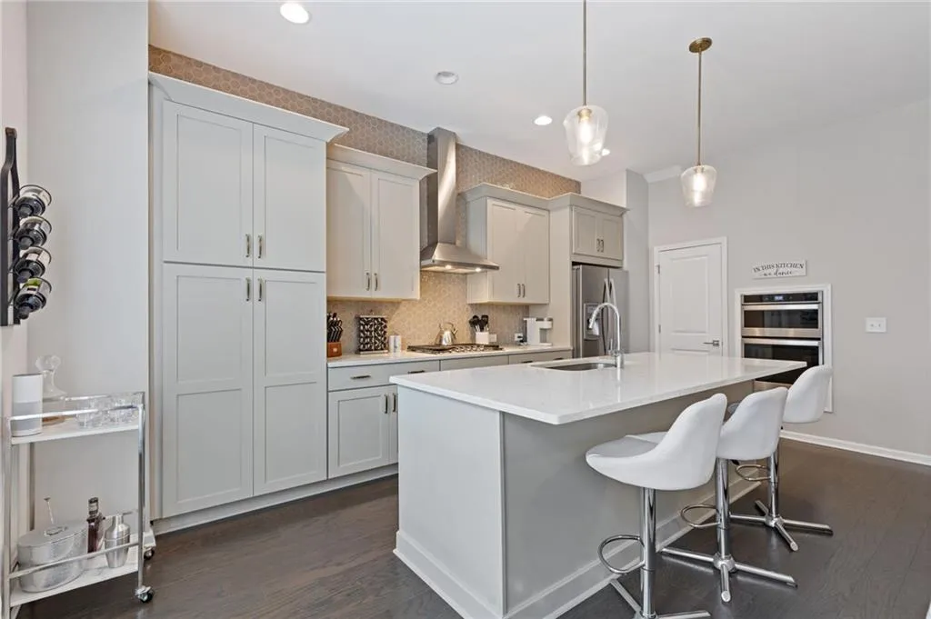 Kitchen with decorative backsplash, dark wood finished floors, pendant lighting, wall chimney exhaust hood, and a breakfast bar